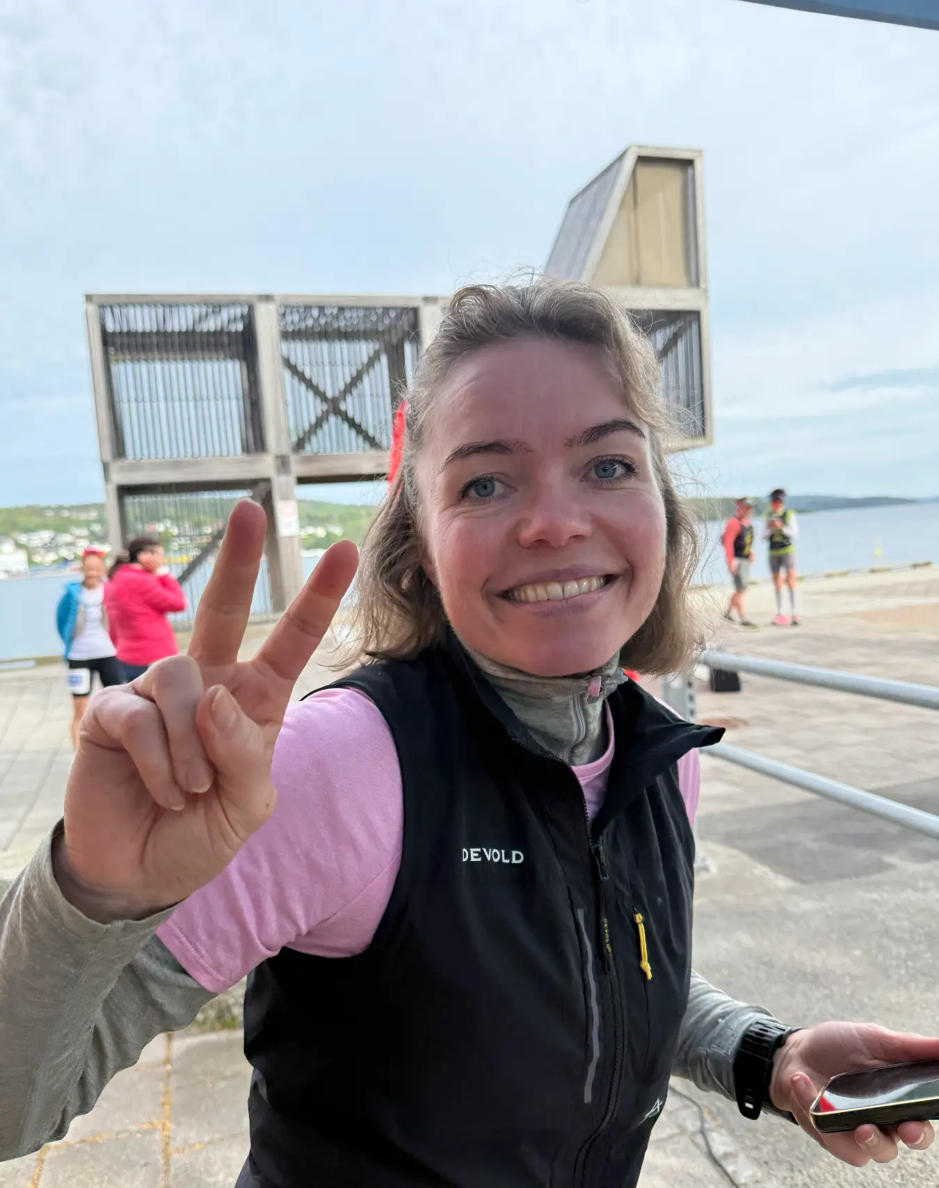Smilende frivillig i Devold-vest ved vannkanten under Endless Shore Ultra Trail